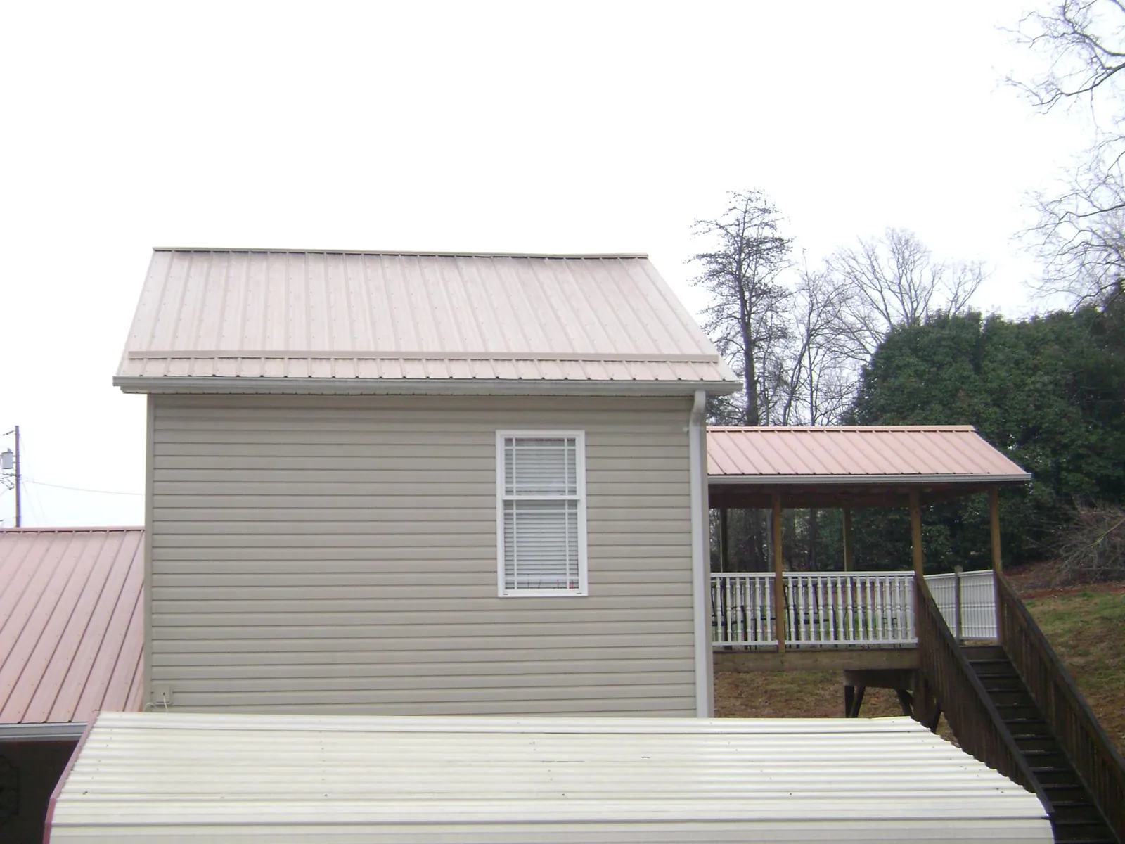 Tan metal roofs on a two story addition and attached porch, from a Roof Replacement job in Middleton